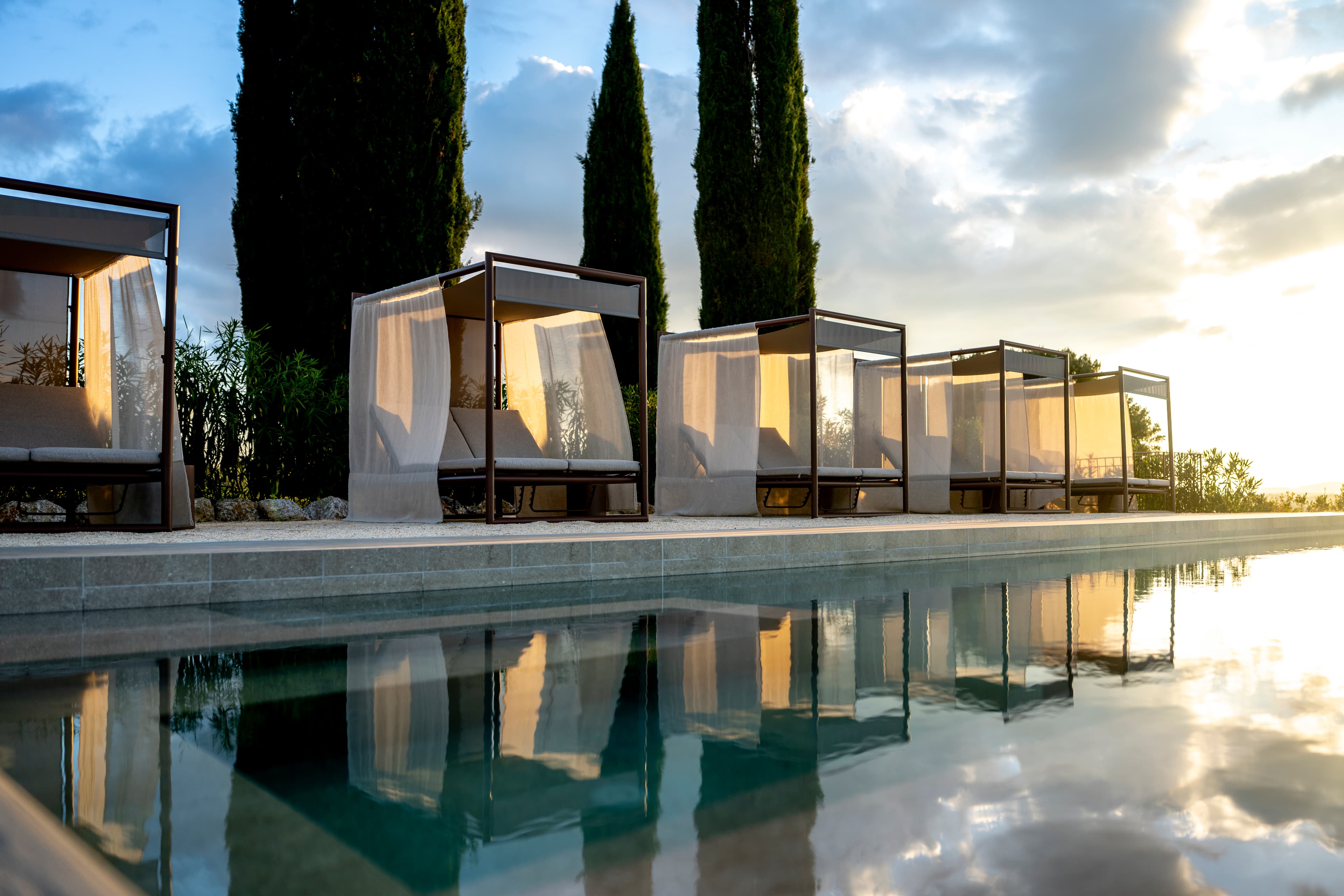 Pool with cabanas and cypress trees at sunset